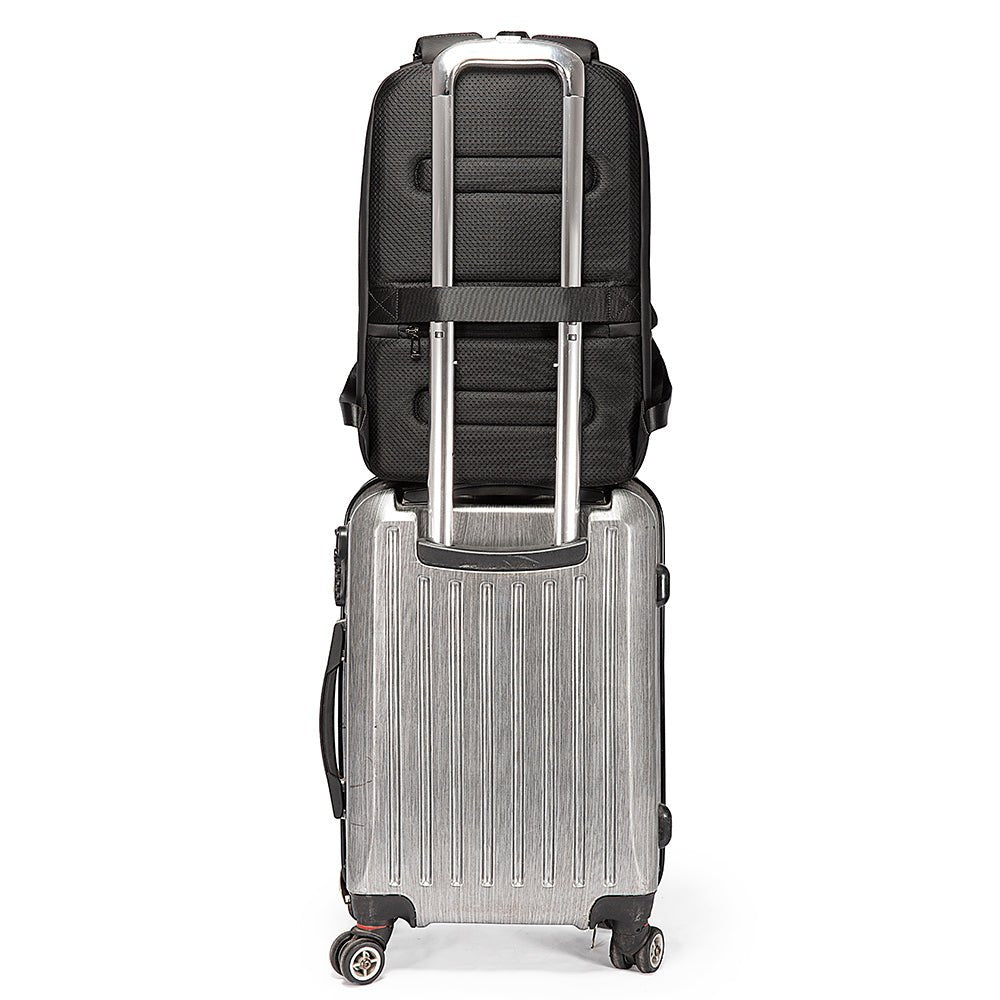Black backpack securely attached to a silver rolling suitcase using rear luggage strap and trolley sleeve.
