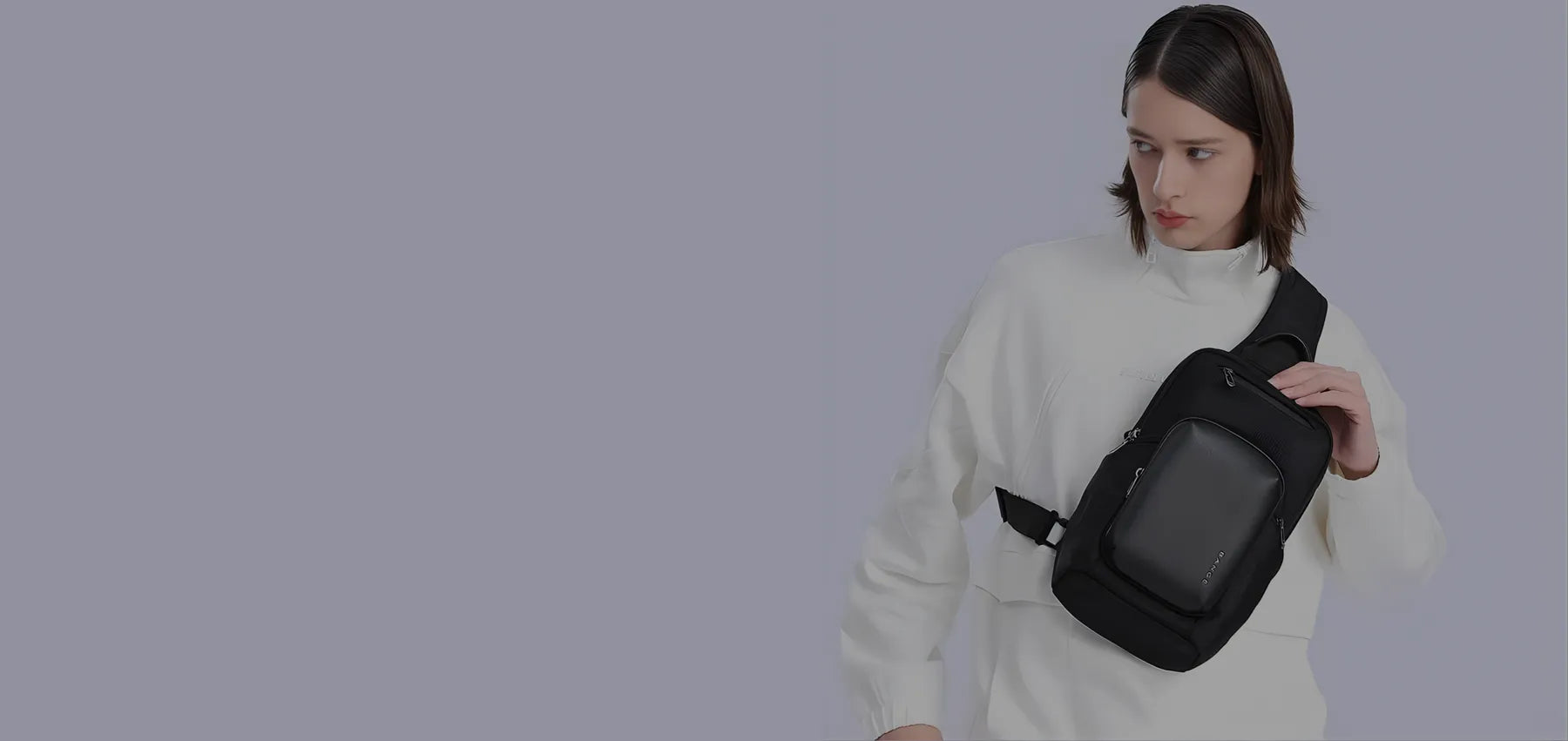 Black crossbody sling bag worn by a model, featuring a minimalist design and compact zippered compartments against a plain background